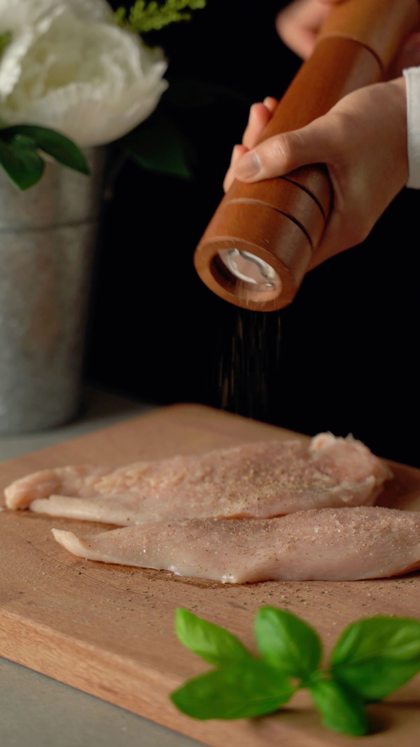 Handen kruiden verse kipfilets met een pepermolen op een houten snijplank